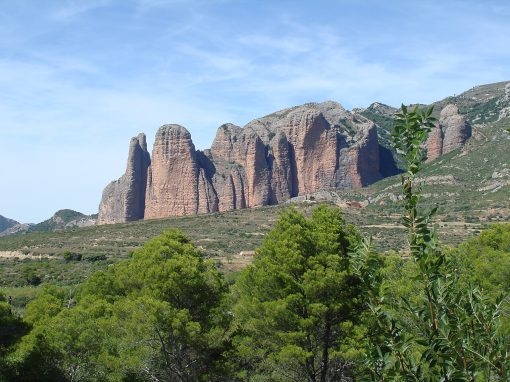 Montañas rocosas conocidas como Mallos de Riglos, rodeadas de vegetación en la Hoya de Huesca